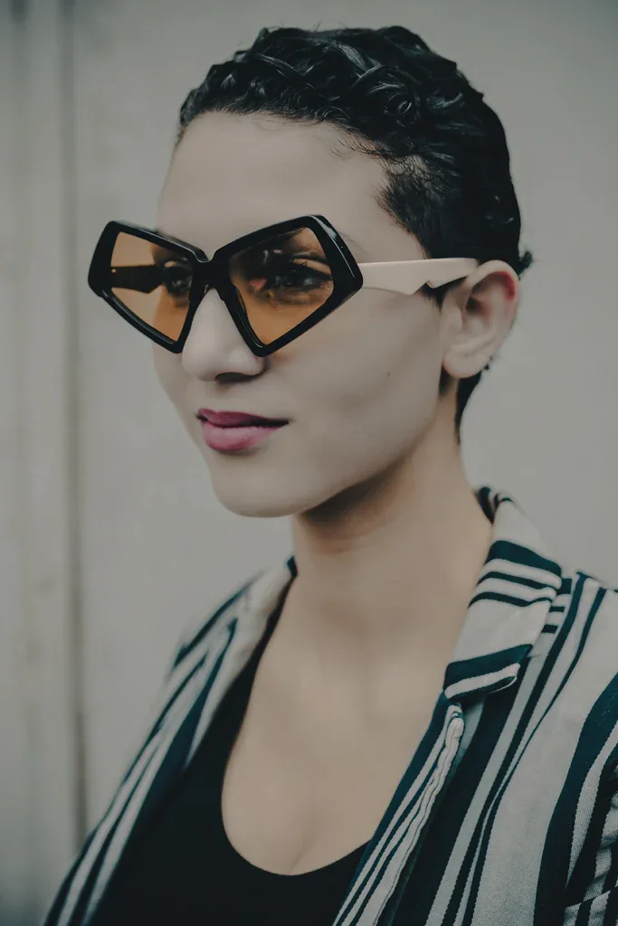 Model in black angular Ffin MOD sunglasses with amber lenses and a striped blazer