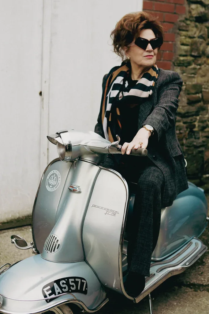 Rose, Anna's mum, in black Ffin MOD sunglasses and a scarf riding a silver vintage scooter