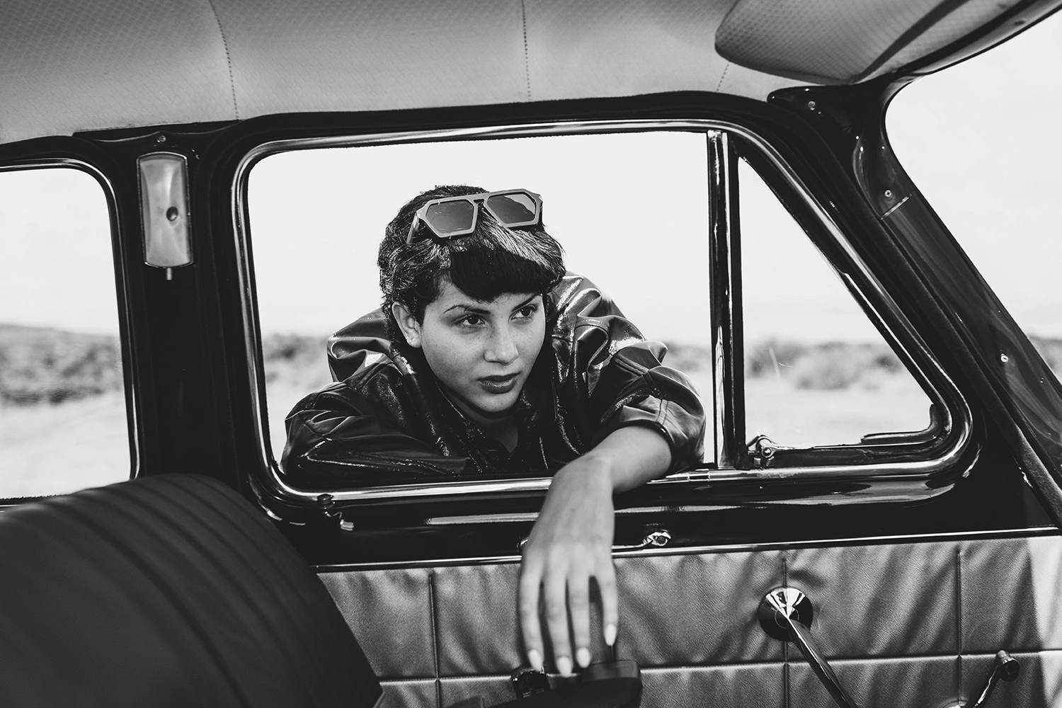 Model with sunglasses pushed up into their hair leaning from a vintage car window, Ffin shoot