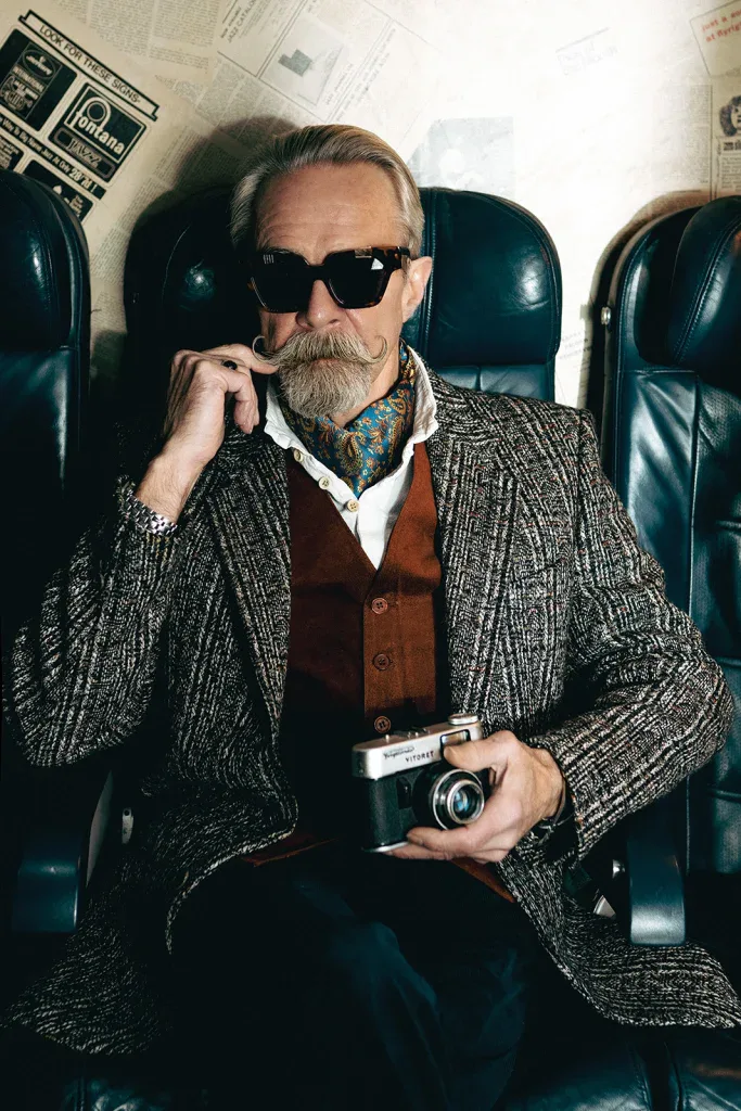 Gary, with a waxed moustache, in black Ffin AMO designer sunglasses holding a vintage camera on a leather seat