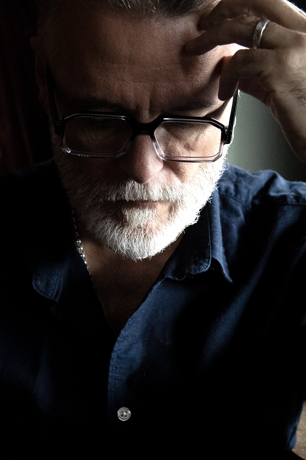 Steve Balsamo in black Ffin BOD optical frames, hand to his temple, in low light