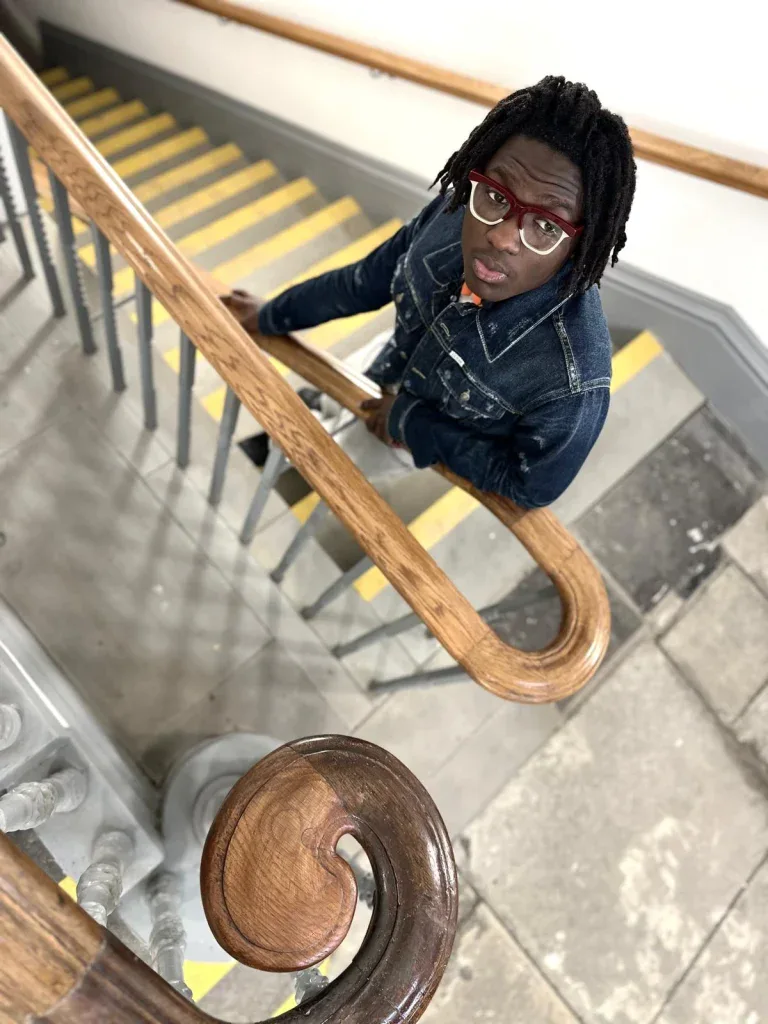 Young man in red Ffin GEN optical frames looking up from a staircase, high-angle view