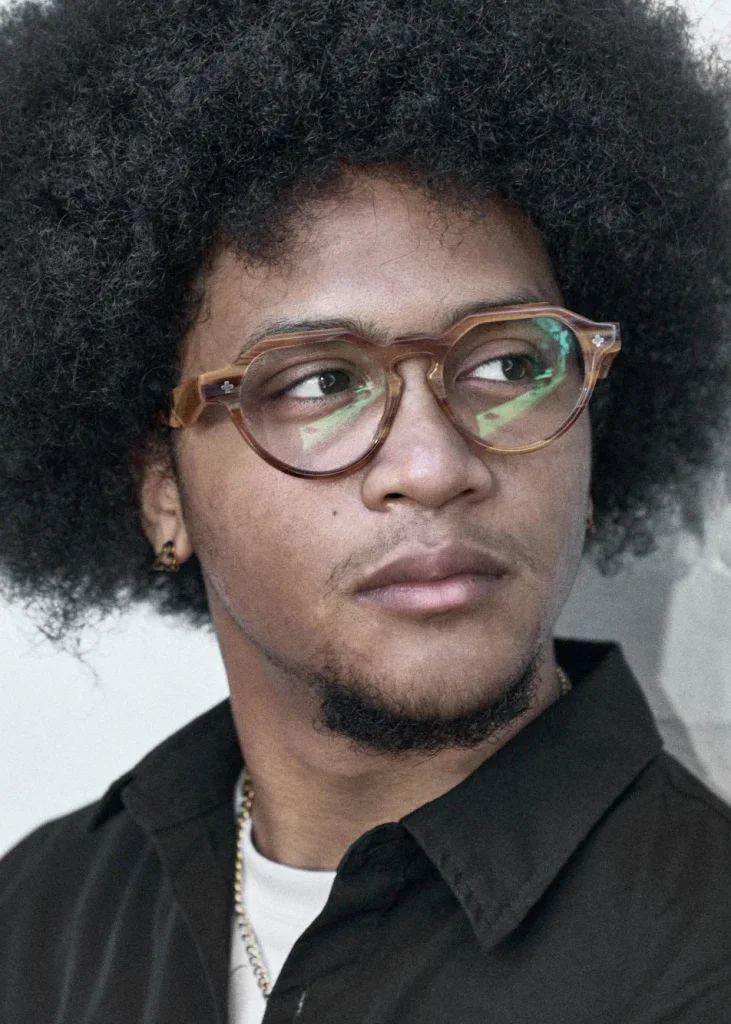 Man with an afro in round amber Ffin NON optical frames, glancing to one side