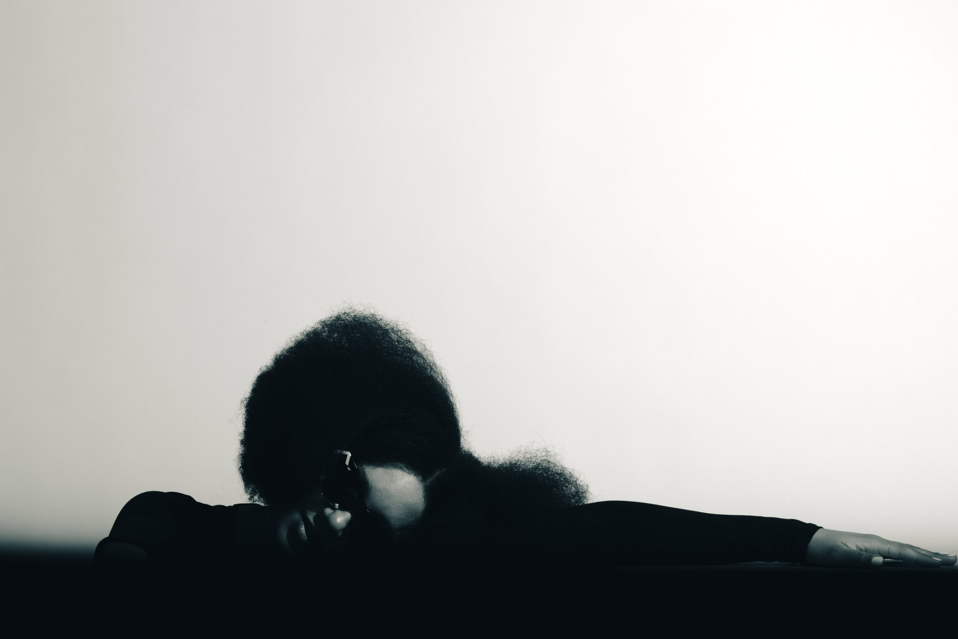 Silhouetted model resting their head on their arms against a bright backdrop, Ffin NOS campaign