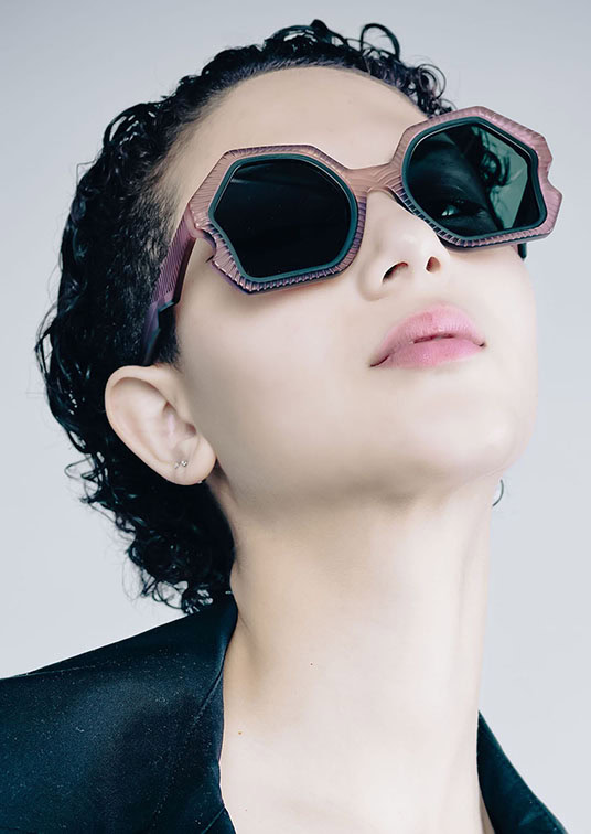 Woman with dark curls looking upwards in hexagonal mauve Ffin AER designer sunglasses