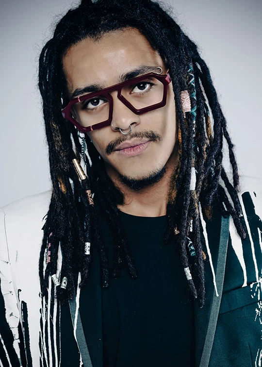 Man with locs in burgundy angular Ffin ERA optical frames and a black and white jacket