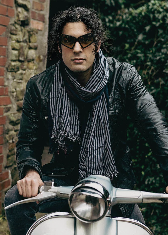 Man in a leather jacket and striped scarf wearing angular Ffin MOD sunglasses on a vintage scooter