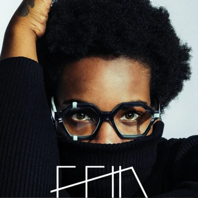 Model in black hexagonal Ffin optical frames with mint details, face half covered by a black roll neck