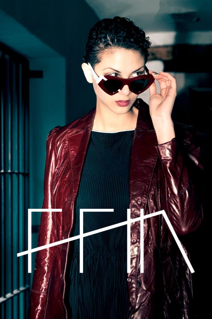 Model lowering red heart-shaped Ffin NOS designer sunglasses in a burgundy patent jacket, with the Ffin logo