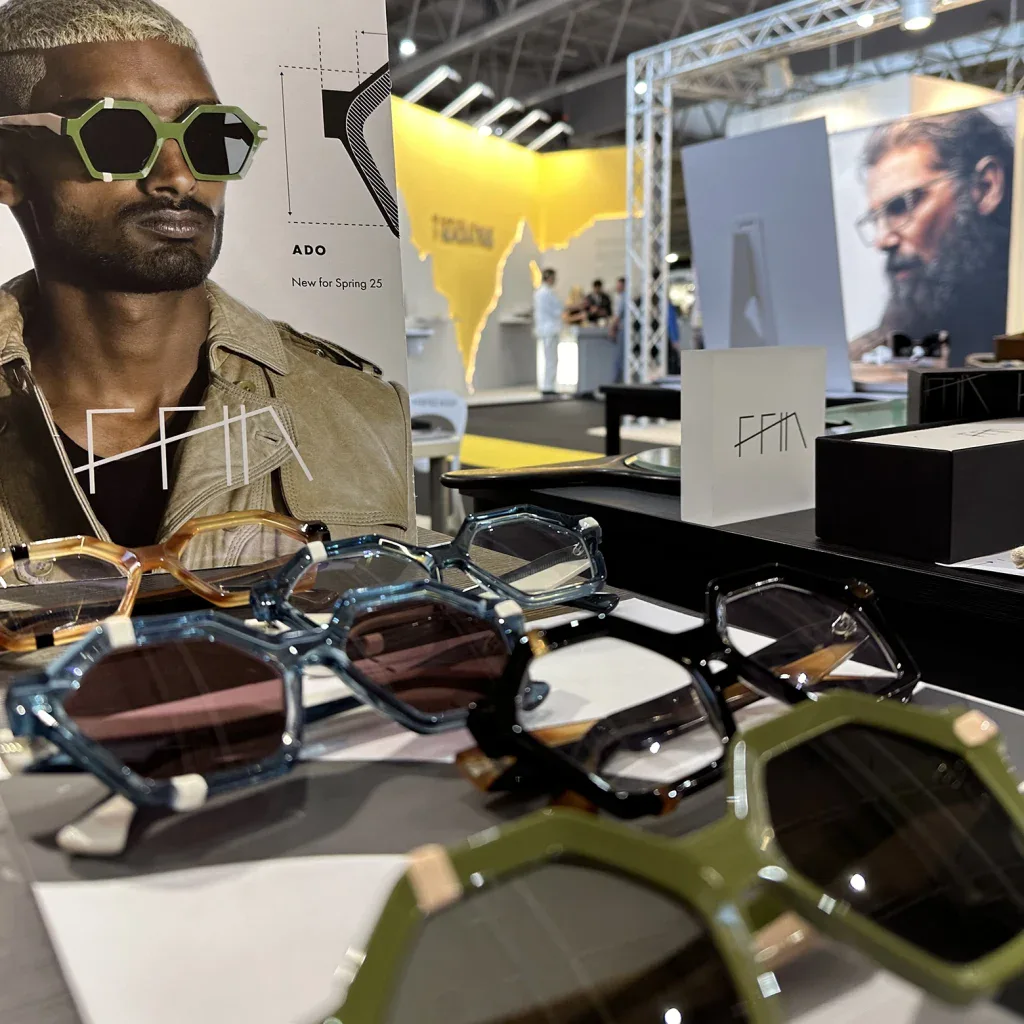 Green hexagonal Ffin ADO designer sunglasses on display beside portrait prints at SILMO