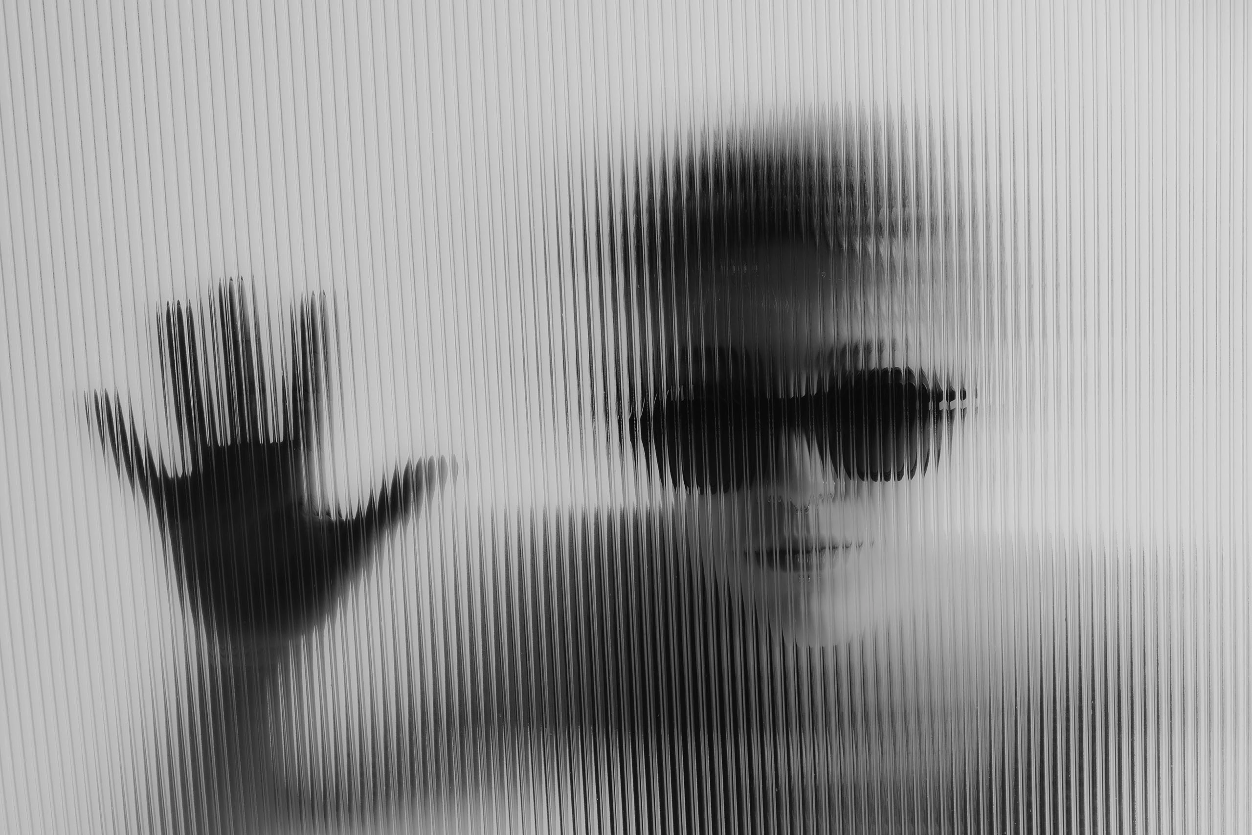 Hand pressed against ribbed glass beside a blurred model in Ffin ANA sunglasses