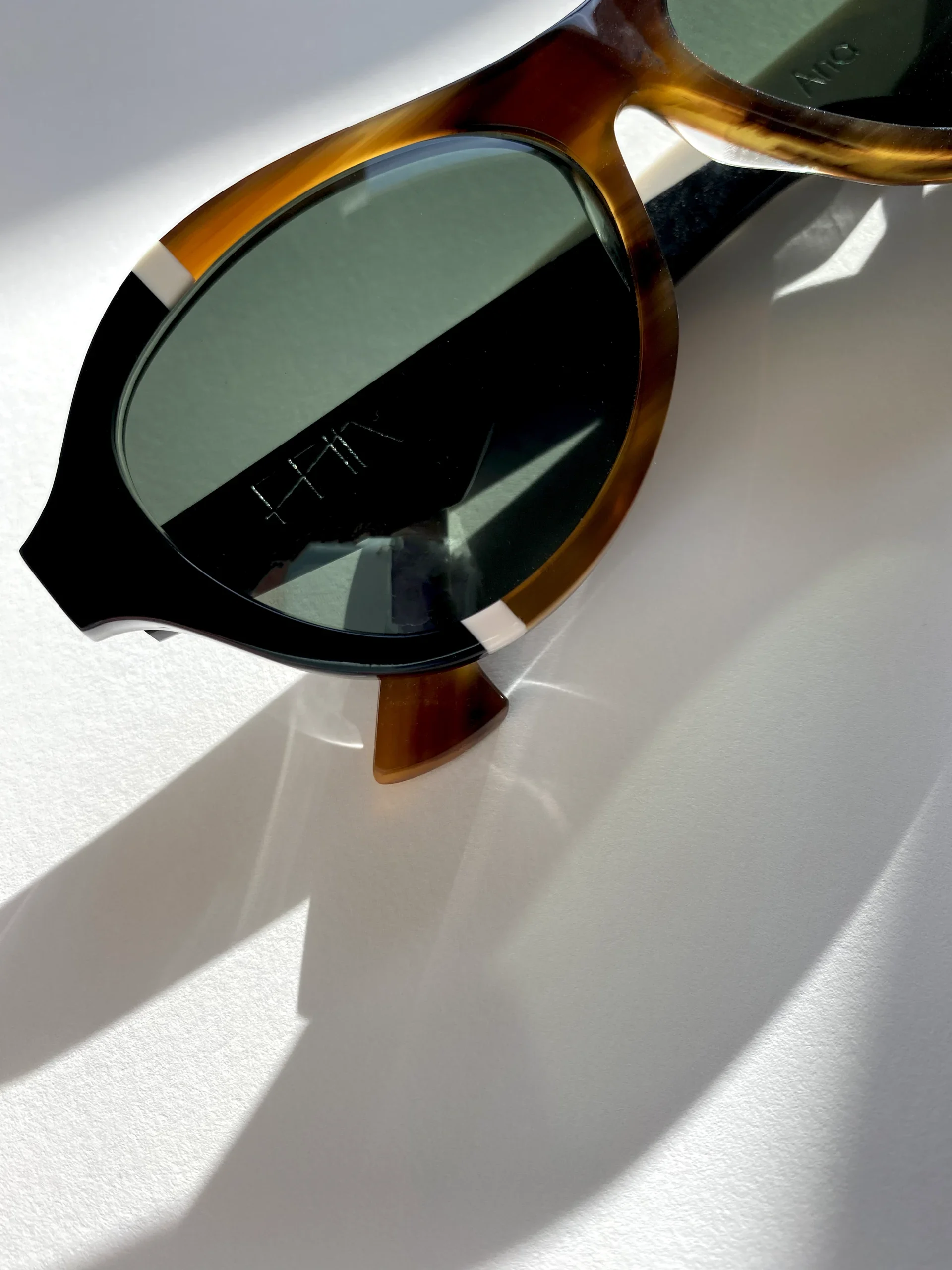 Close-up of tortoiseshell Ffin ANA designer sunglasses with white inlays on a white surface