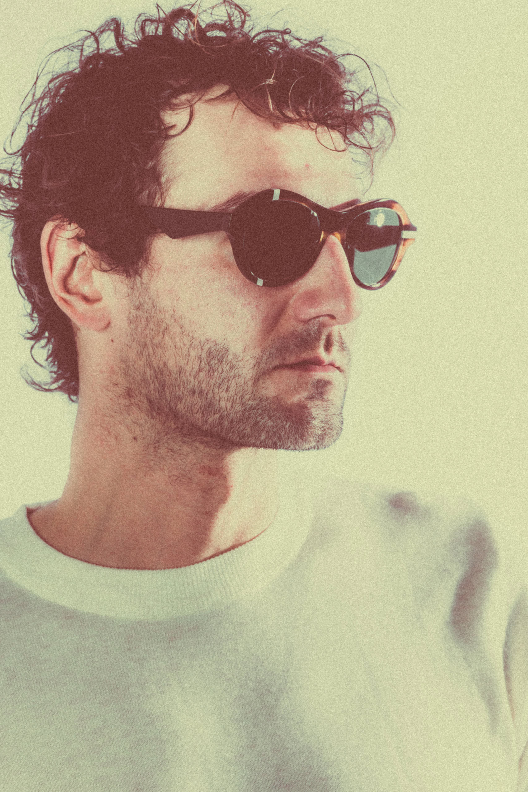 Man with dark curls in round Ffin ANA designer sunglasses, warm sepia-green tone