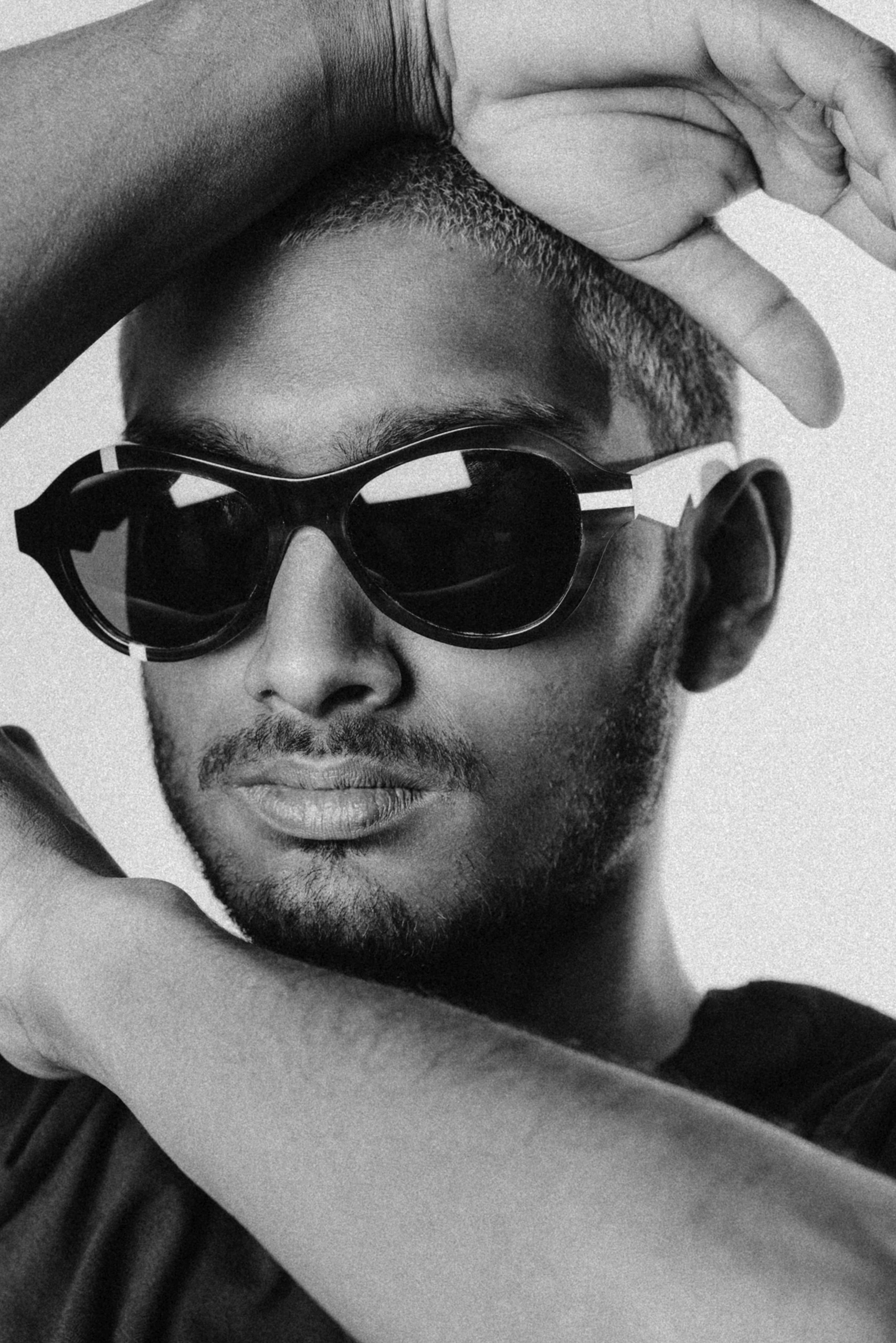 Close black and white portrait of a man in round Ffin ANA sunglasses with white details, arm raised