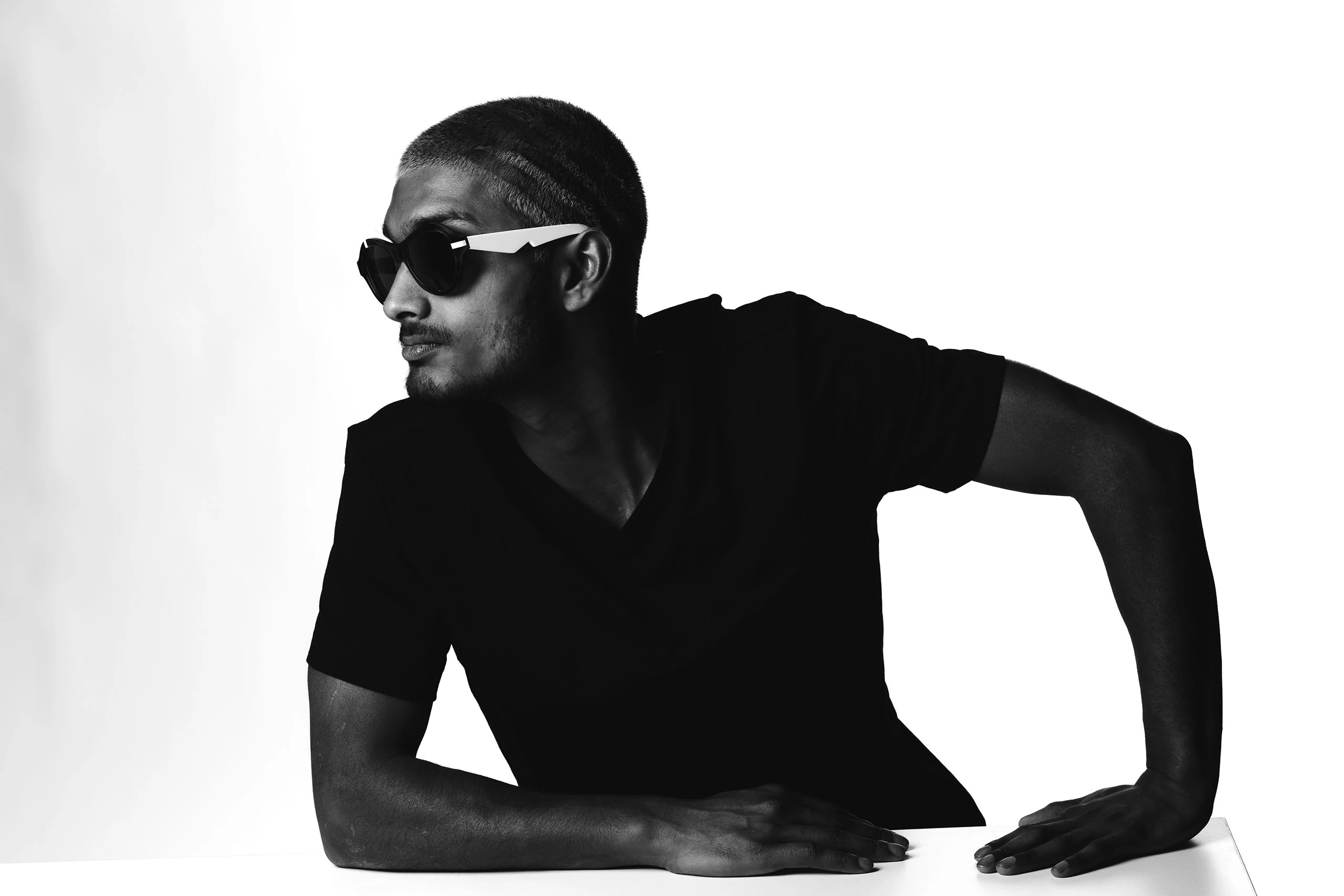 Man in a black t-shirt and Ffin ANA award-winning sunglasses leaning on a table, looking left