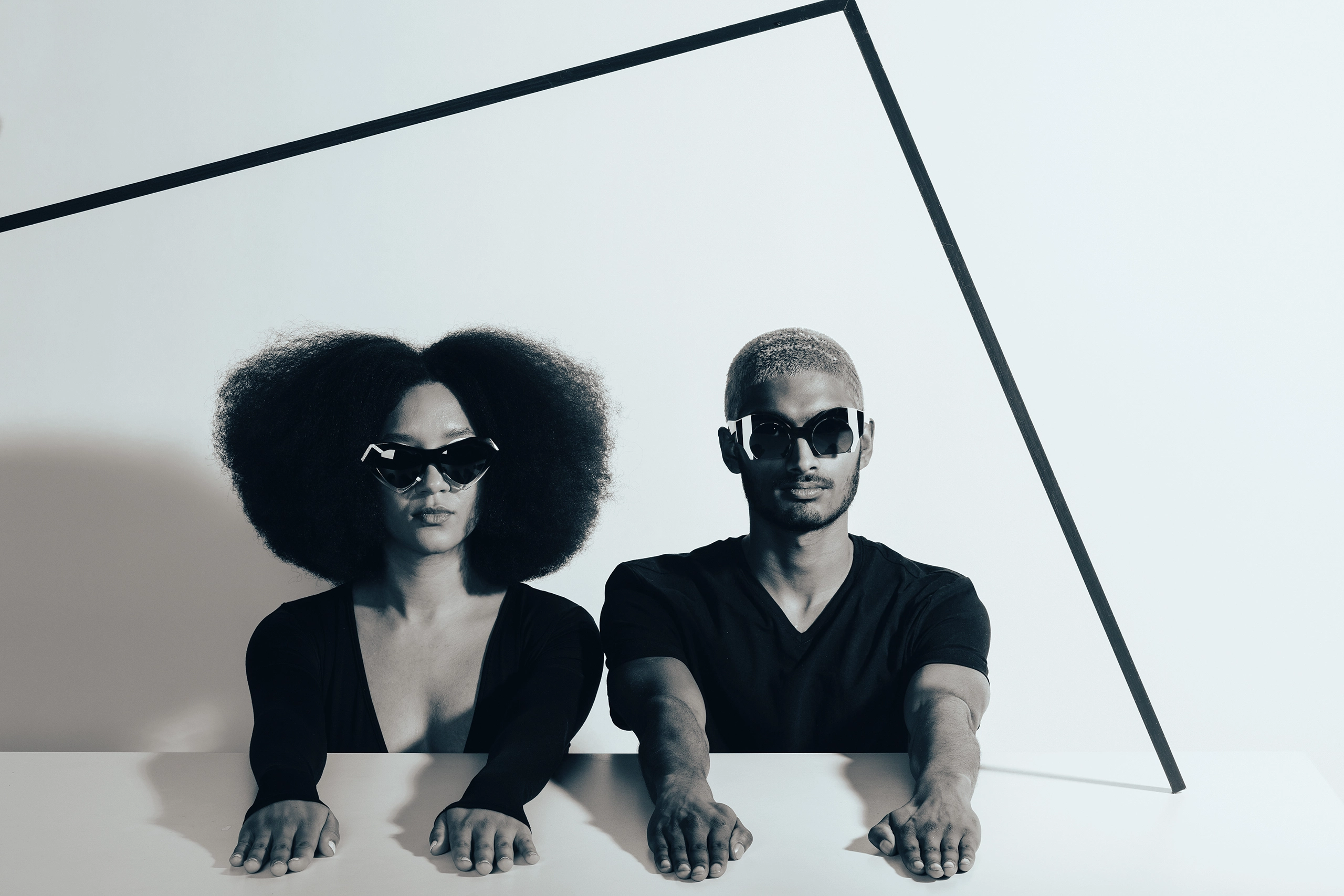 Two models in Ffin designer sunglasses behind a white table crossed by a black line, the Start Line shoot