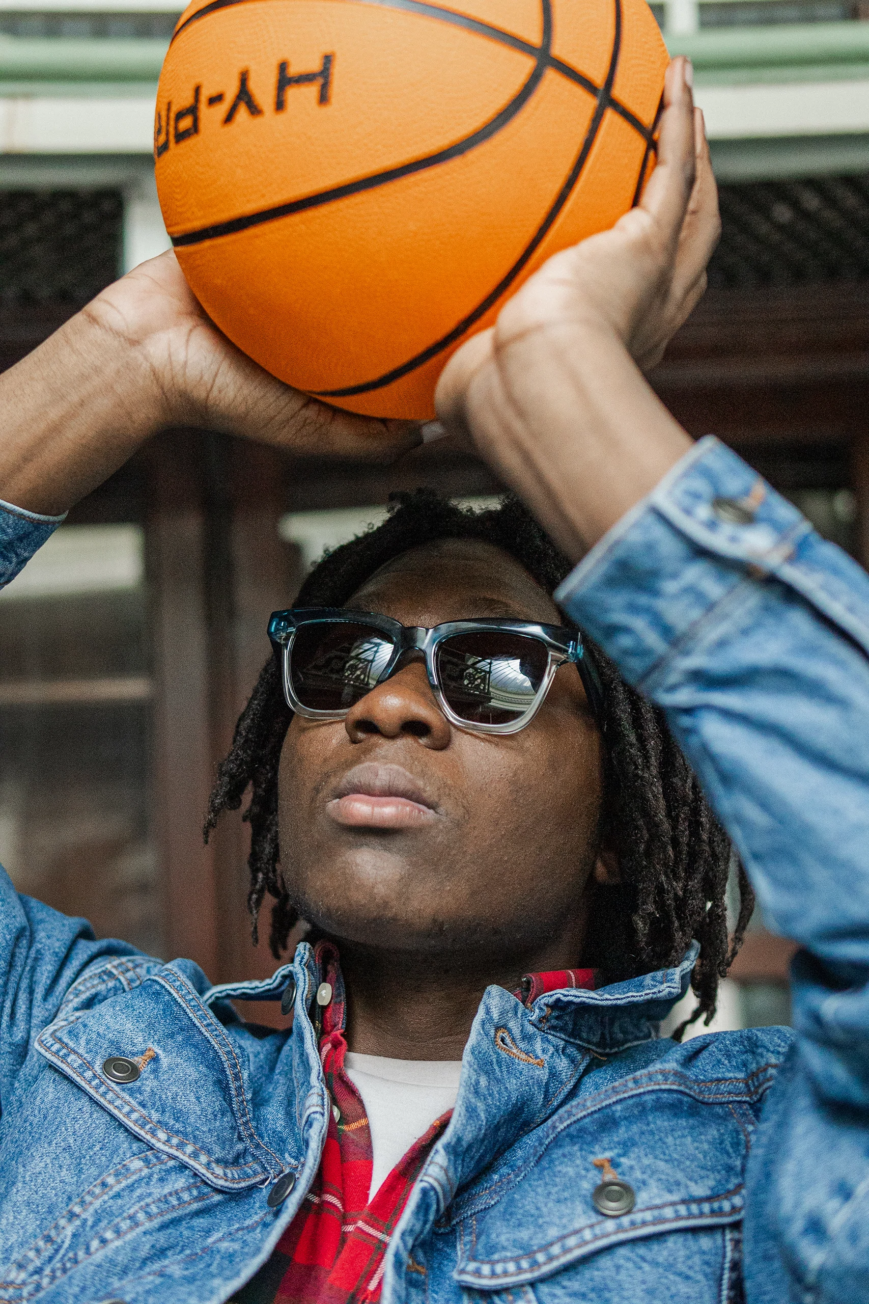 Young man in Ffin GEN blue sunglasses and a denim jacket holding a basketball overhead