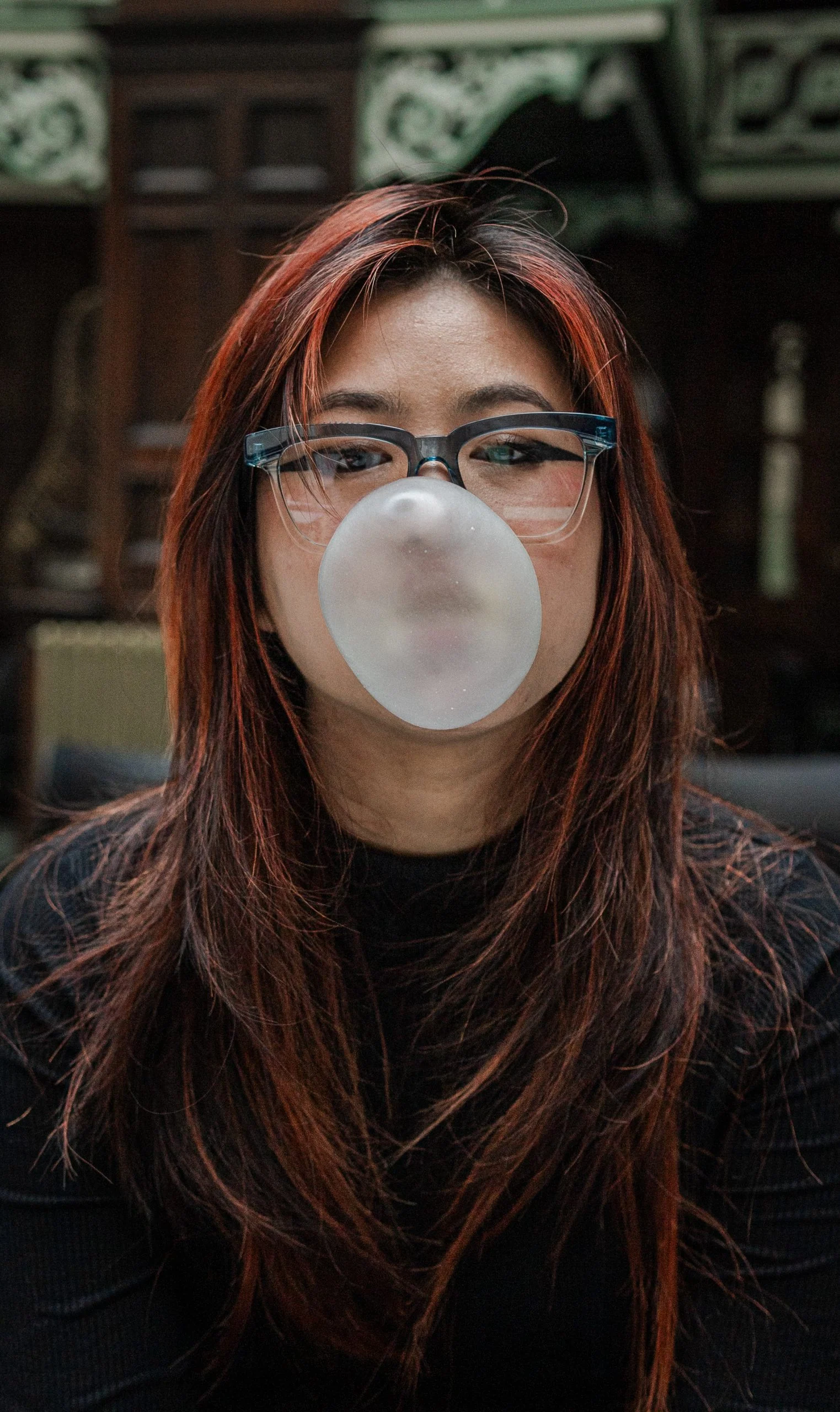 Woman with red-brown hair blowing a bubblegum bubble in black Ffin GEN optical frames