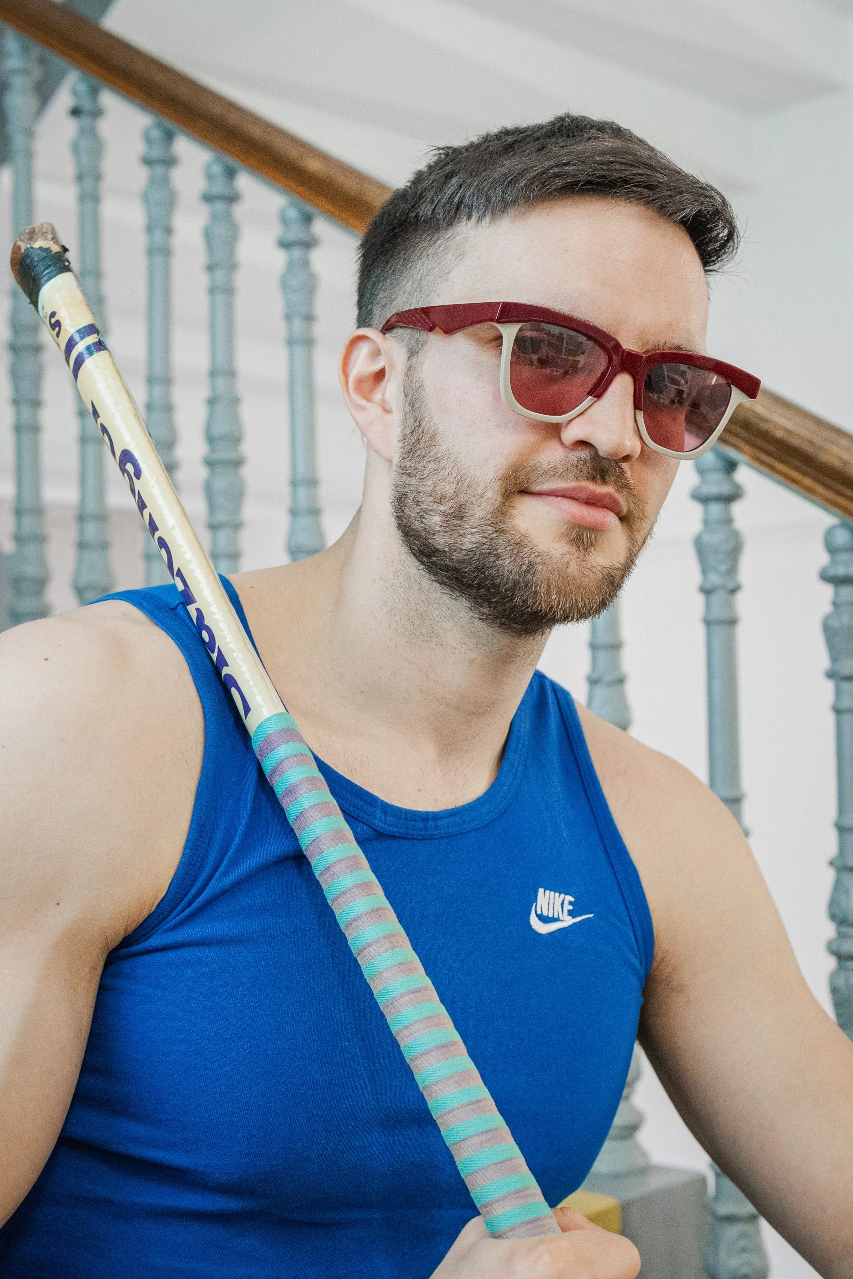Man in a blue vest and red Ffin GEN sunglasses holding a hockey stick on a staircase