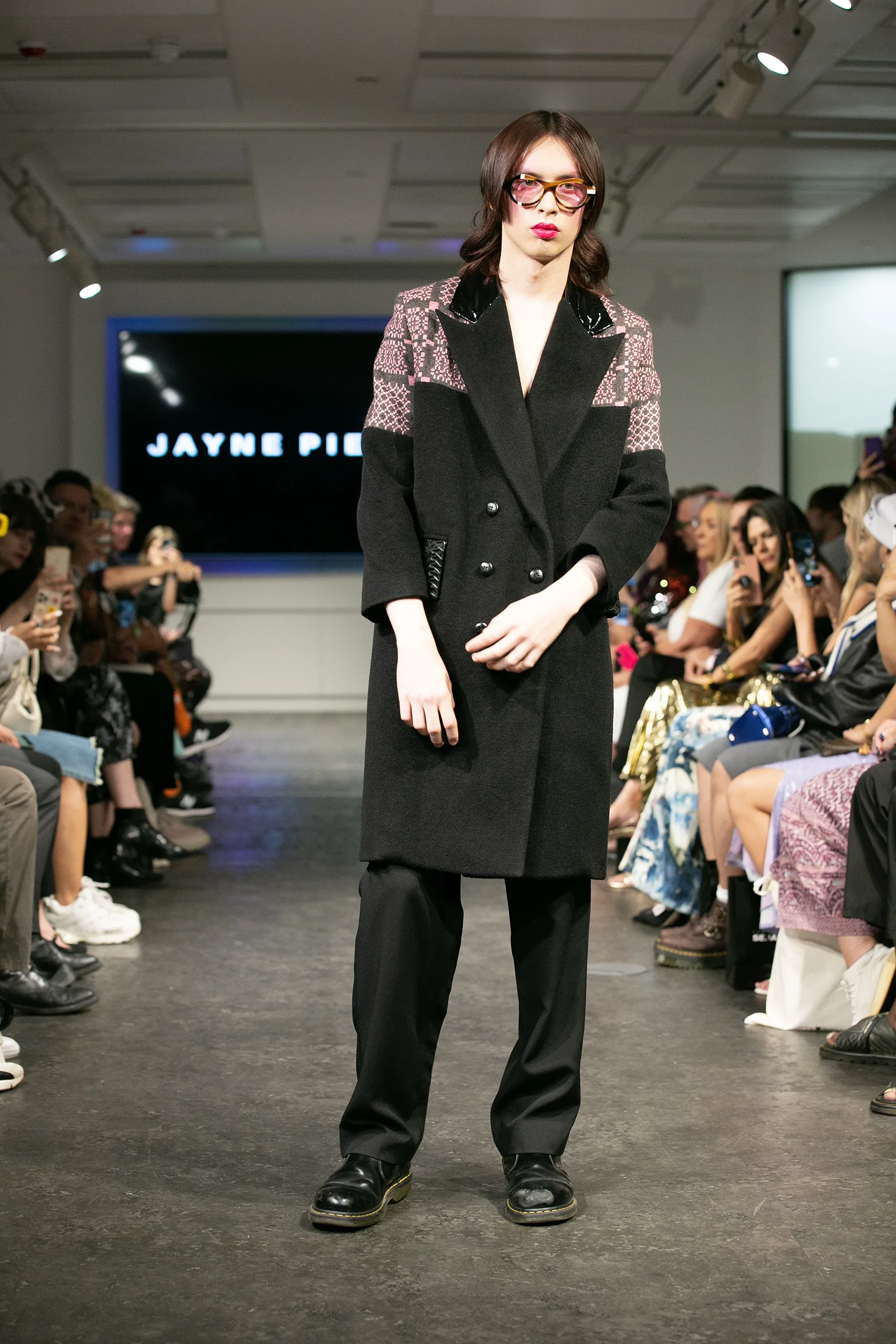 Model in a black coat with pink patterned panels and Ffin ANA sunglasses on the Jayne Pierson catwalk
