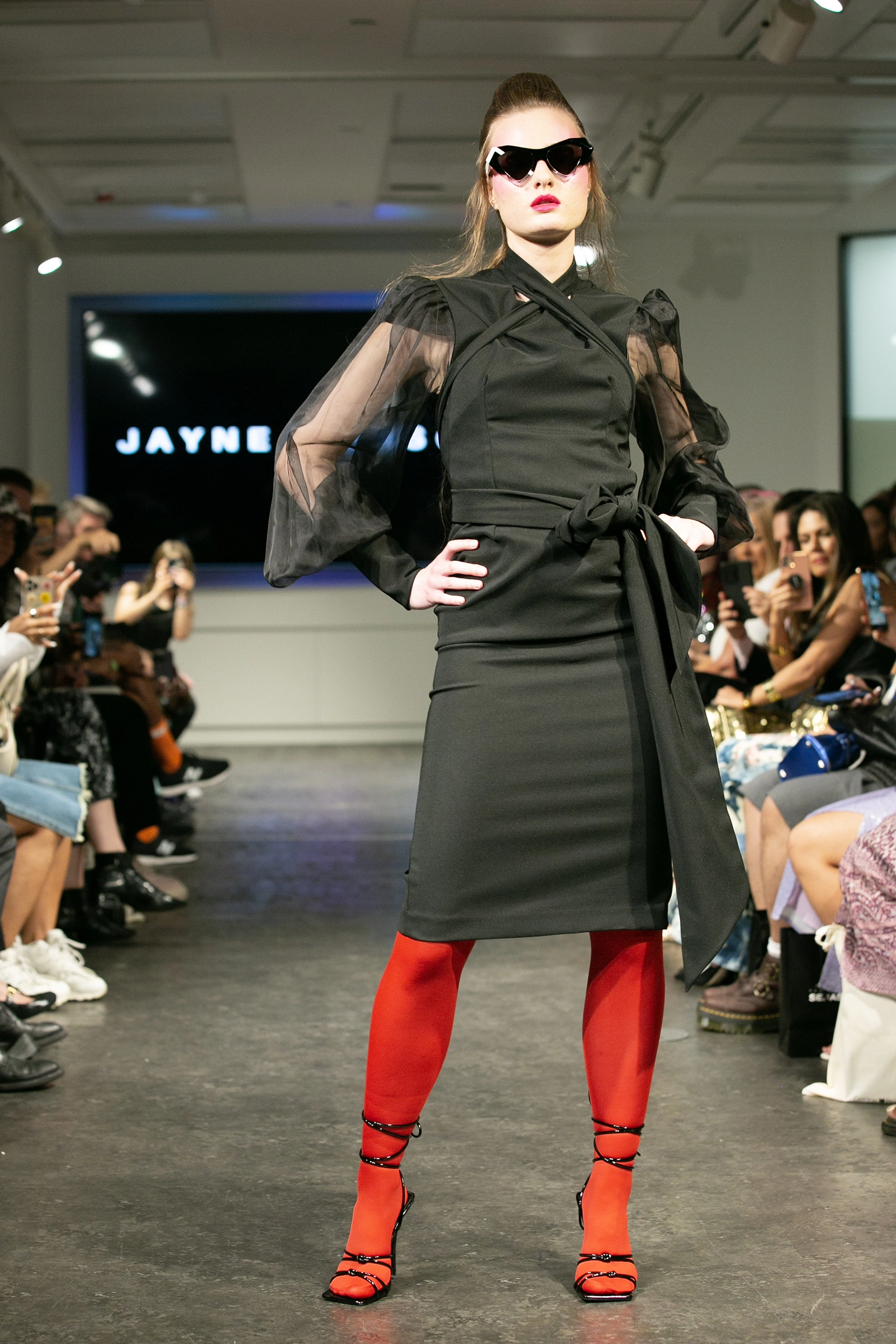 Model in a black dress and red tights on the Jayne Pierson catwalk wearing Ffin designer sunglasses