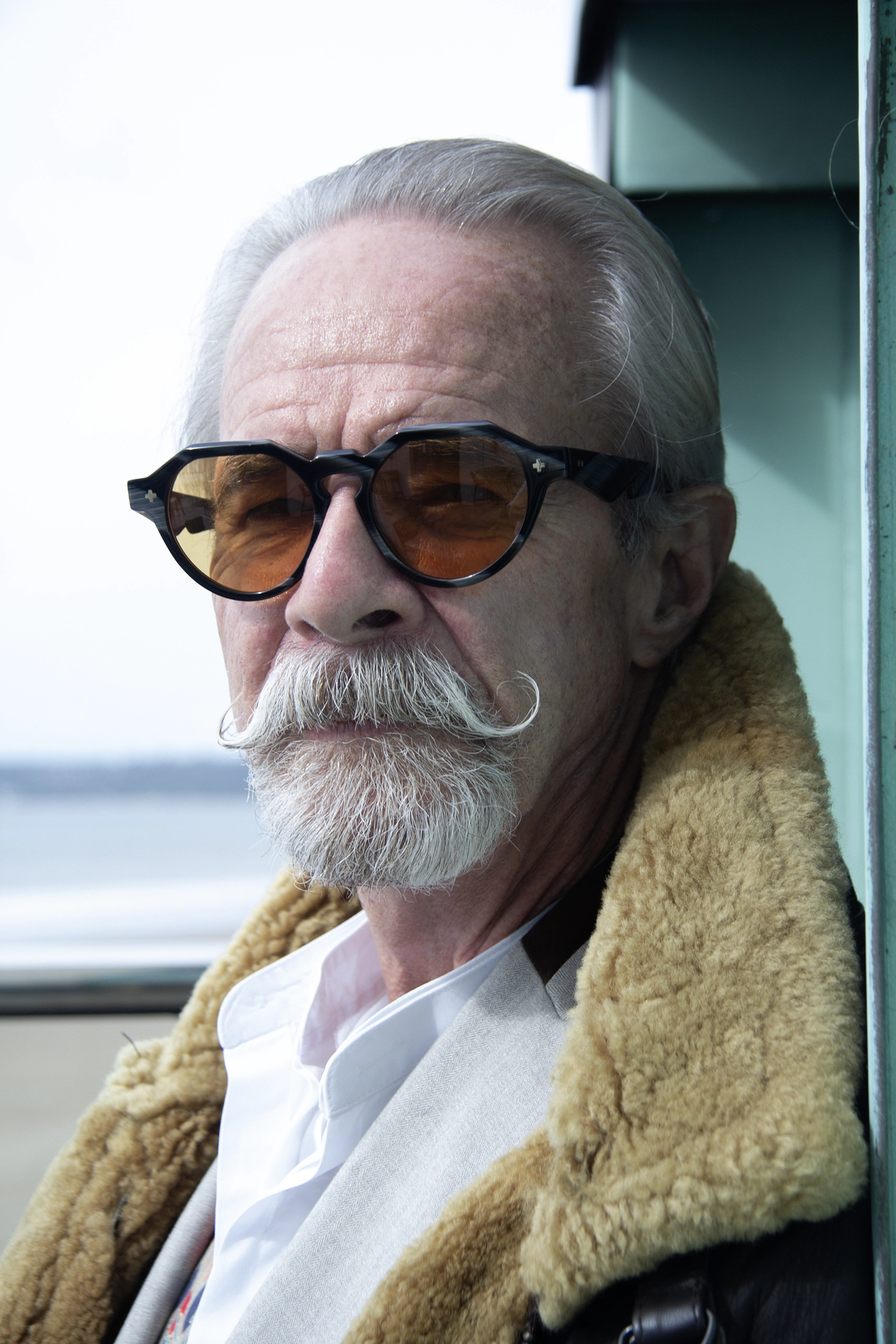 Gary with a waxed moustache in black Ffin NON designer sunglasses with amber lenses and a shearling collar