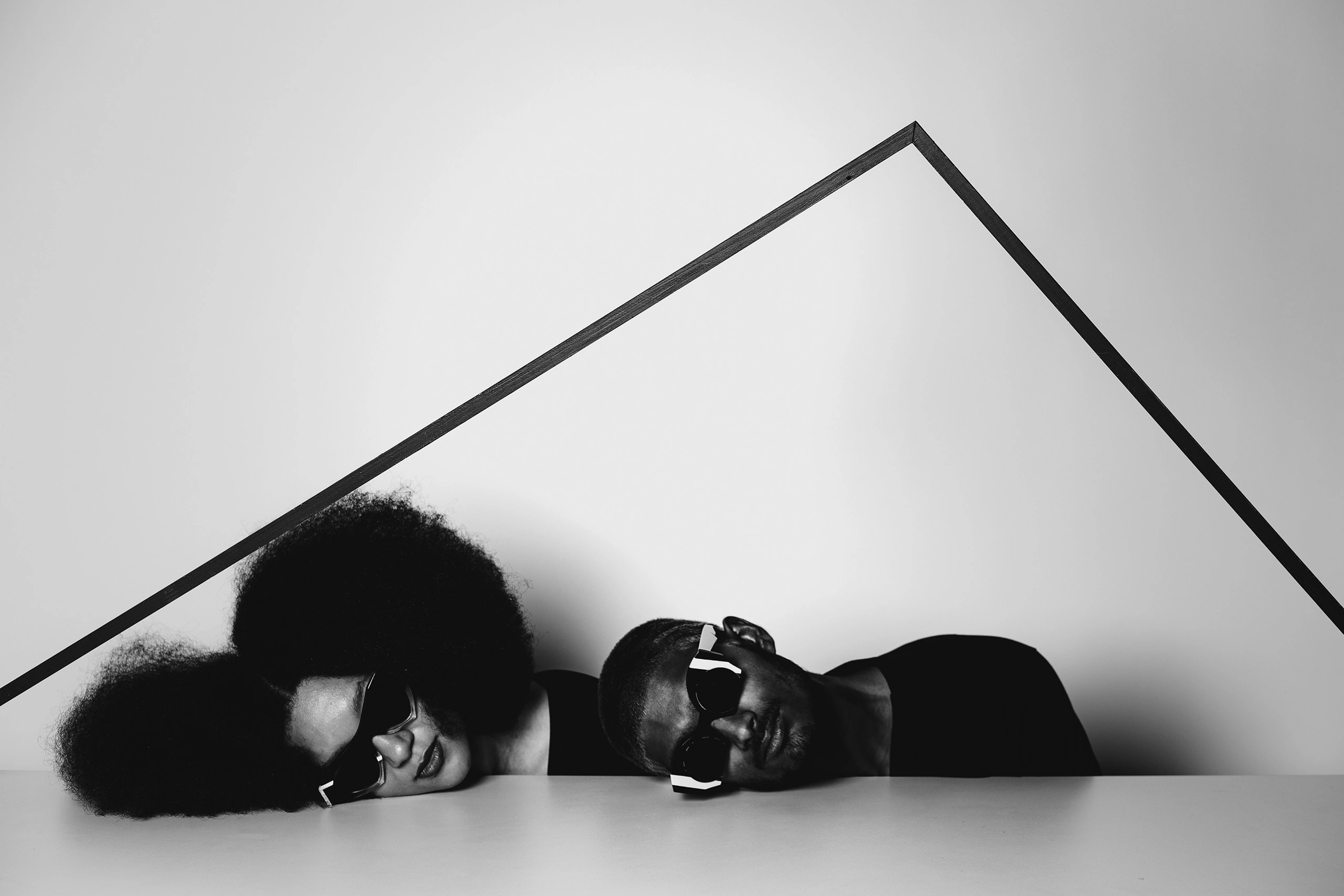 Two models resting their heads on a table in Ffin NOS and ORA sunglasses beneath a black line