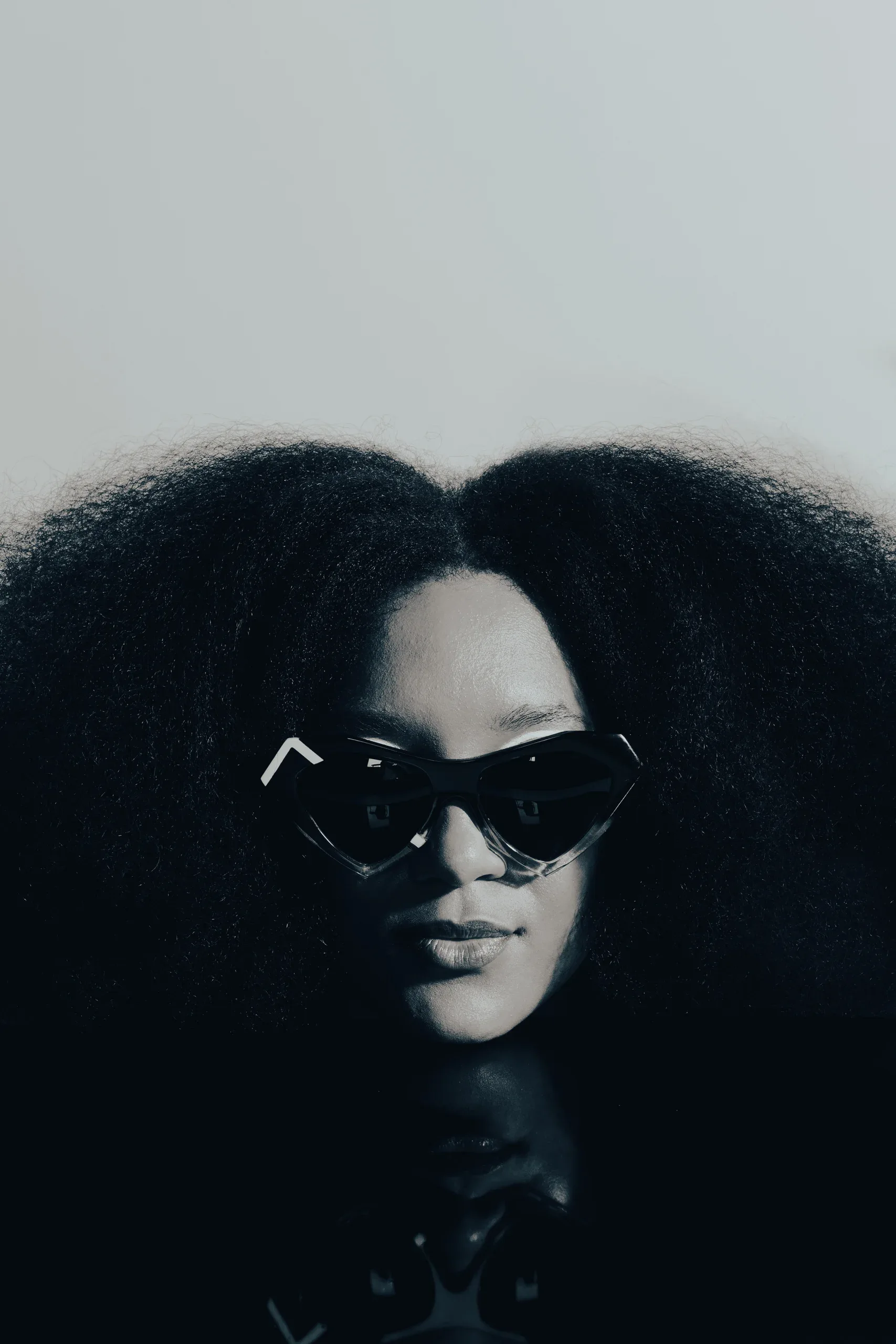 Woman with a large afro in black heart-shaped Ffin NOS designer sunglasses, moody studio portrait