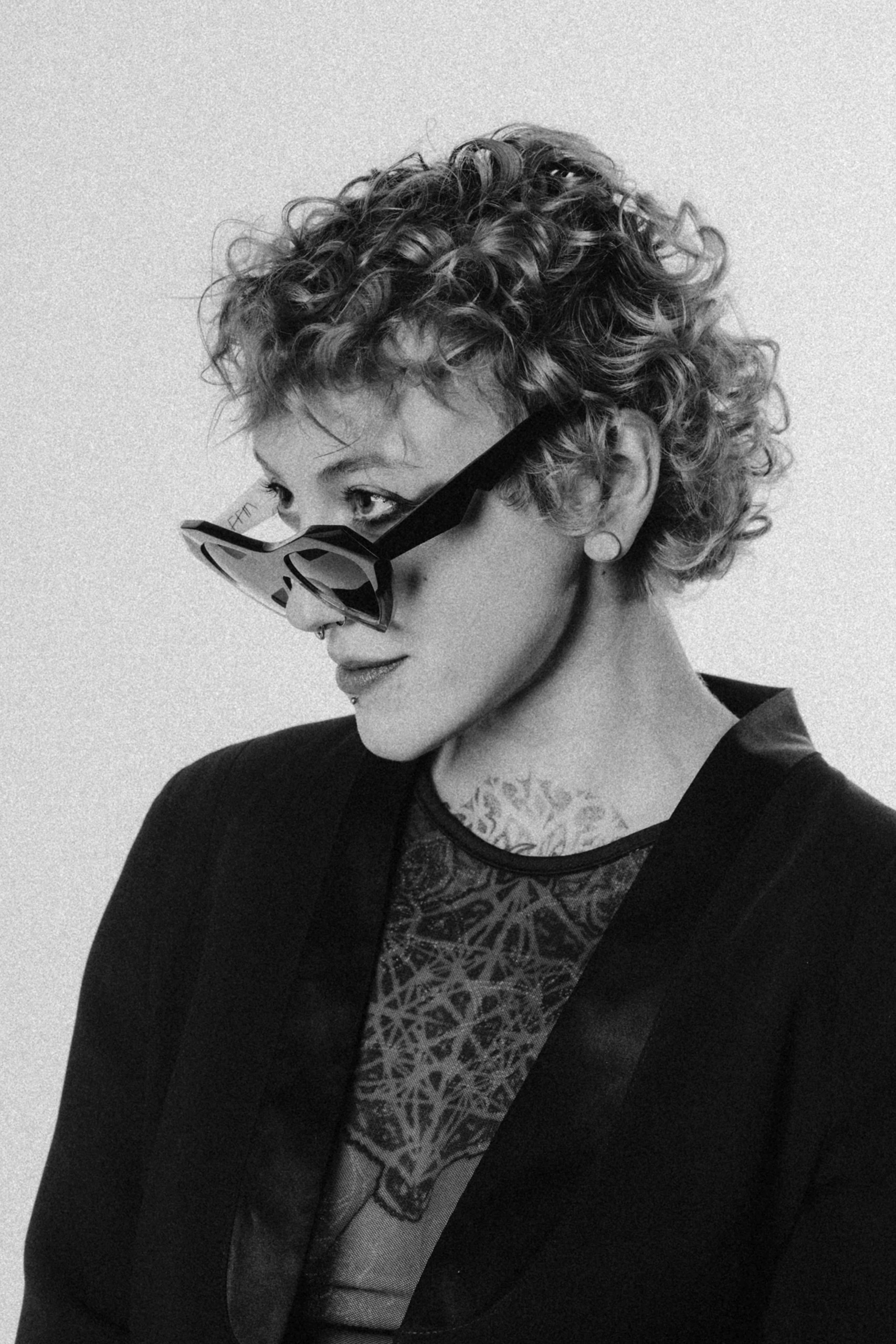 Black and white portrait of a woman with curly hair tilting black Ffin NOS sunglasses down her nose