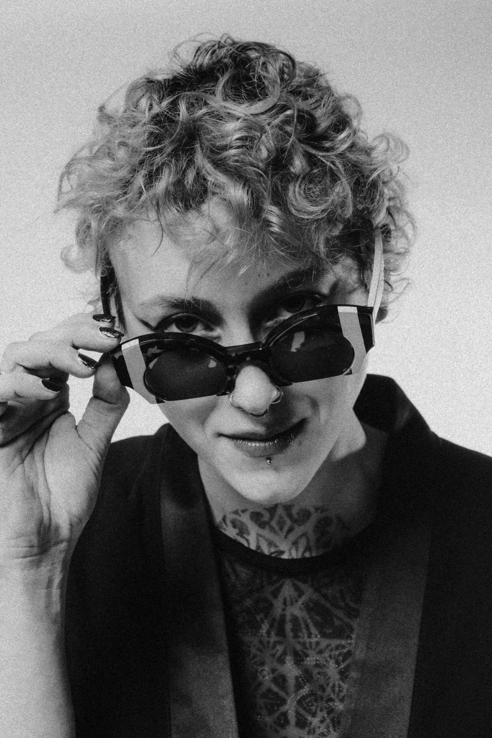 Black and white portrait of a model with curly hair lowering Ffin ORA designer sunglasses