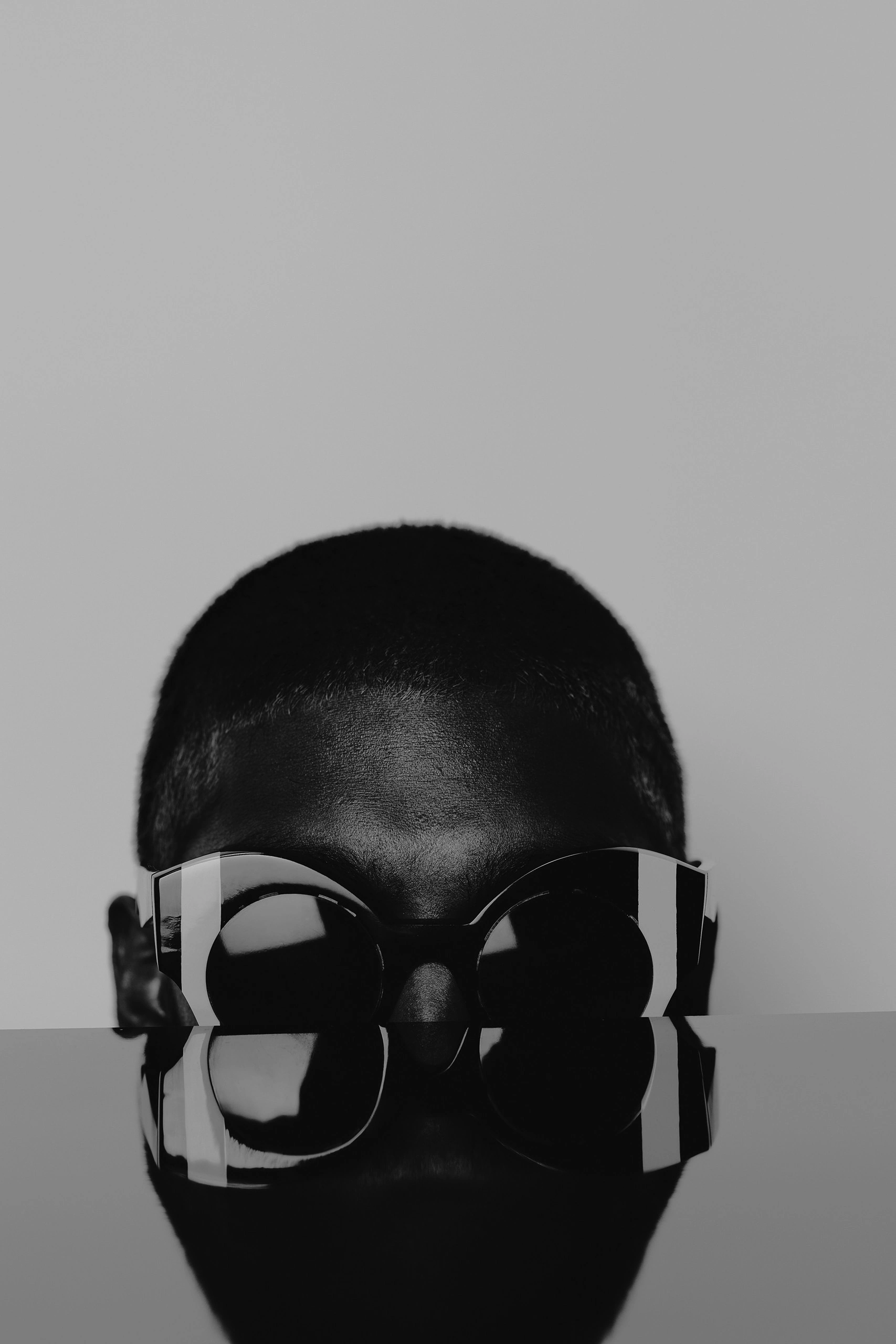 Model with a shaved head in bold black and white Ffin ORA designer sunglasses, reflected in a glossy table