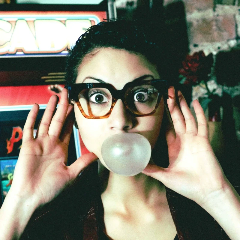 Woman in black and tortoiseshell Ffin AMO optical frames blowing a bubblegum bubble