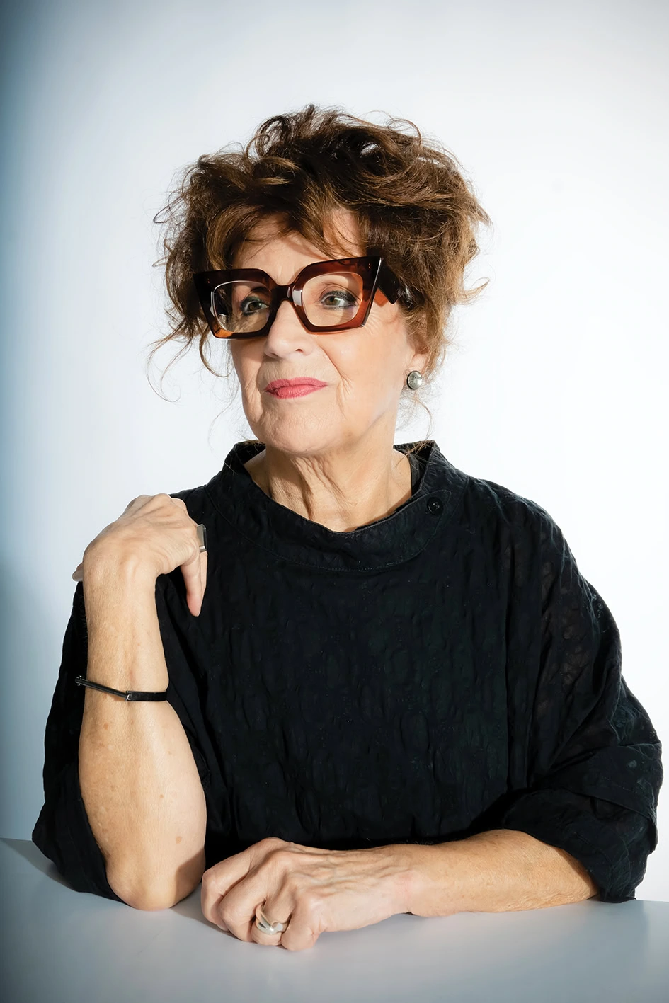 Rose in red and black Ffin optical frames and a black top, smiling with hands folded